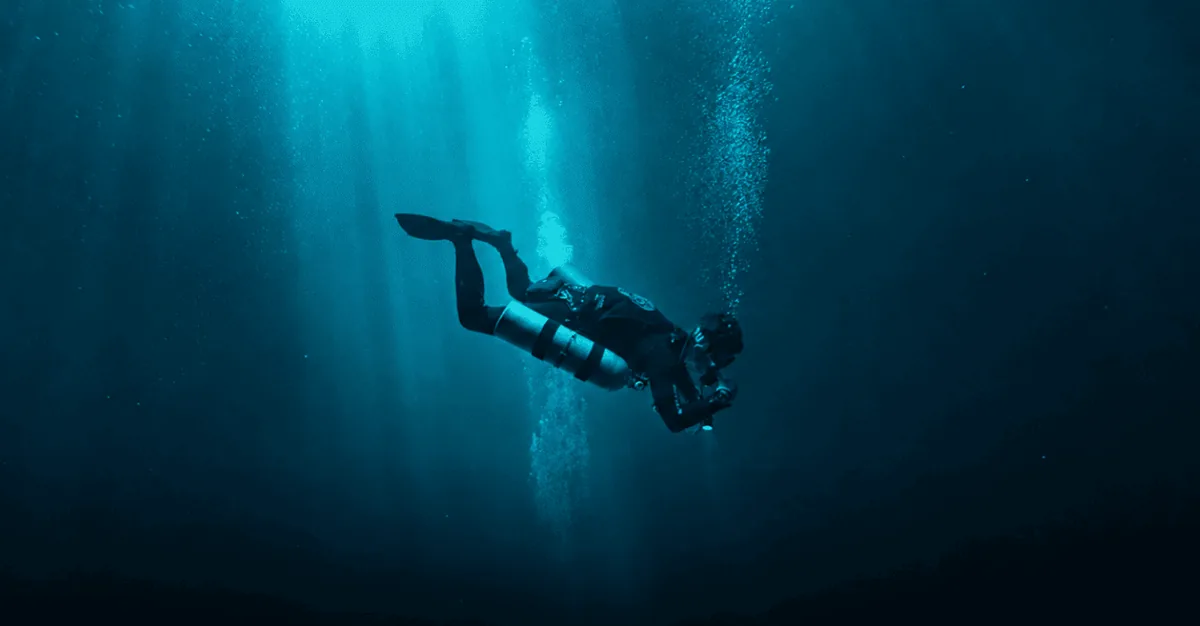 Scott Finch diving sidemount in Gran Canaria, silhouetted in blue water with bubbles rising