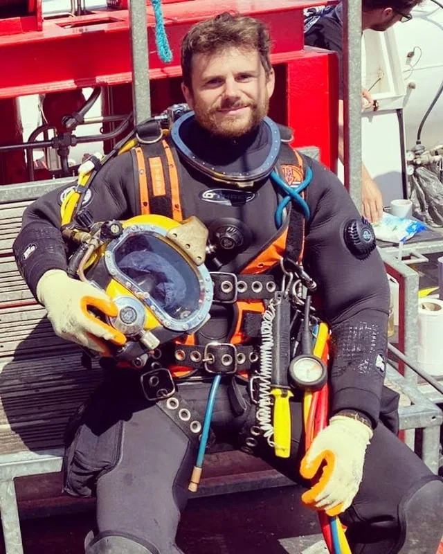 Scott Finch in commercial diving equipment holding a dive helmet